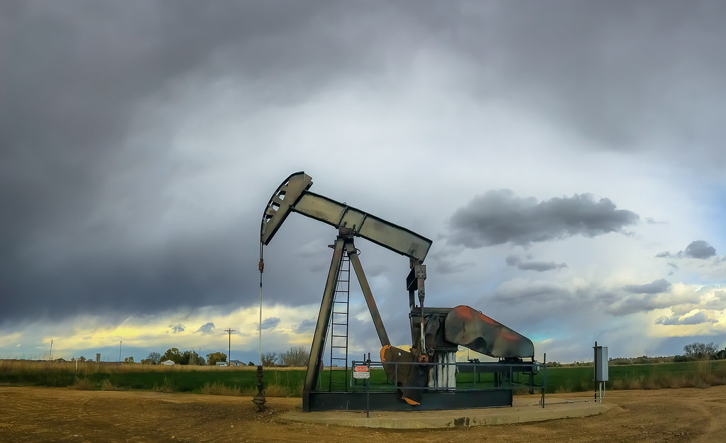 Oil well in a green field in Weld County, Colorado against a backdrop of cloudy skies.