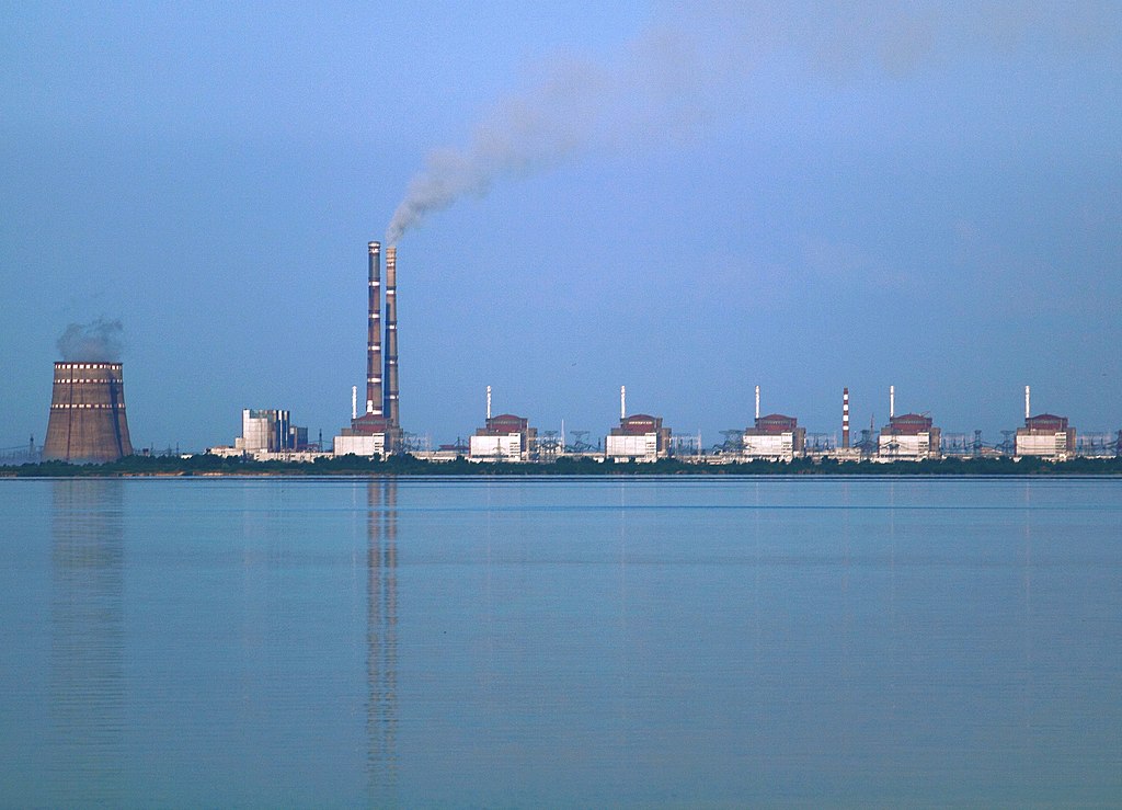 Two power stations at Enerhodar, about 50 km from Zaporozhye in Ukraine, viewed from across the Kakhovka Reservoir on the river Dnieper. Photo taken from the "Nikopol" shore. The nearer power station is Zaporizhzhia Nuclear Power Plant, the biggest nuclear power station in Europe, consisting of two cooling towers (one largely obscured by the other) at the left and 6 VVER reactor buildings. The large building between the cooling towers and the reactors, and the two tall smokestacks, are at the Zaporizhzhia thermal power station about 3 km beyond the nuclear plant.