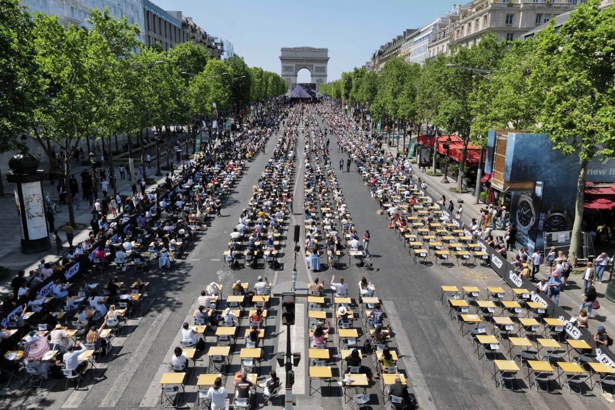 Long shot from the air of participants sitting at desks on the Champs-Elysees prepare to take part in the Big Dictation.