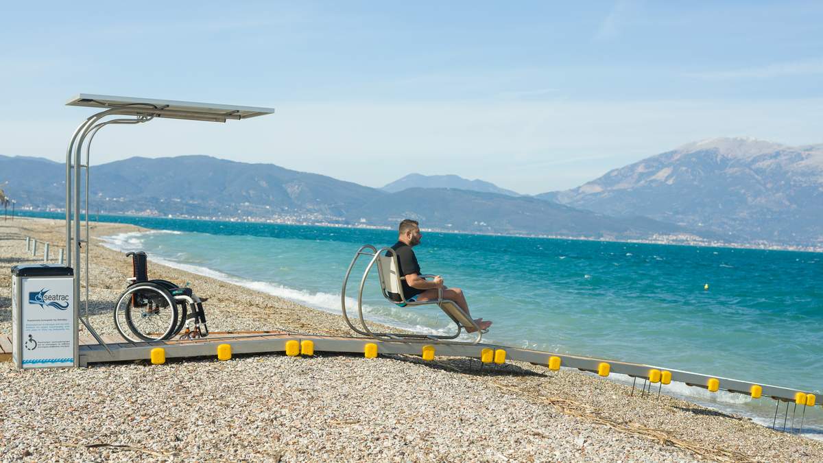 A man rides toward the sea in the chair of the Seatrac system. His wheelchair remains on the beach.