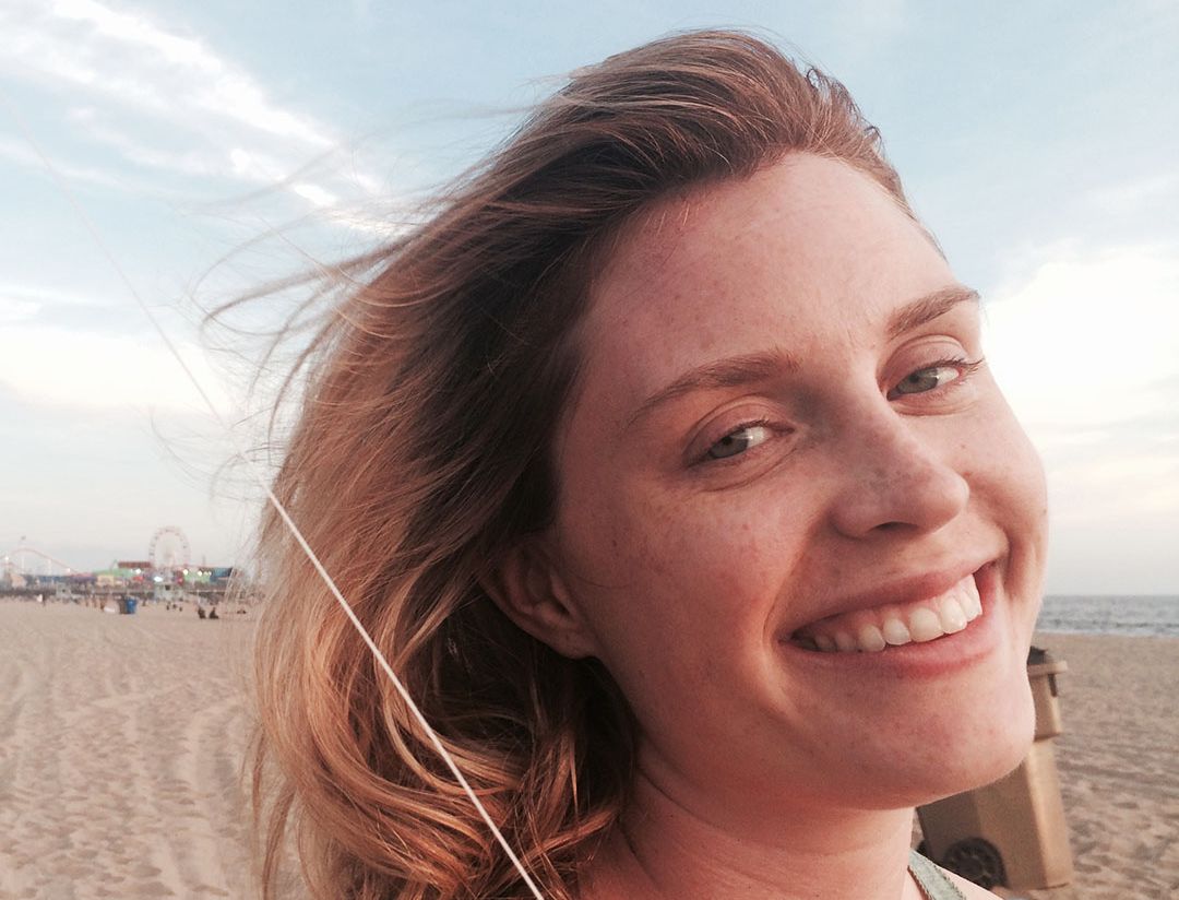 A picture of Casey McIntyre smiling at the camera at the beach.