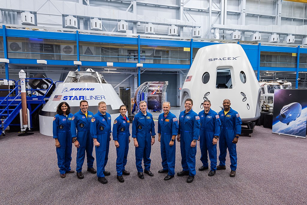 The first U.S. astronauts who will fly on American-made, commercial spacecraft to and from the International Space Station, pose for a portrait in front of the Boeing CST-100 Starliner and SpaceX Dragon Commercial Crew vehicle mock ups at NASA's Johnson Space Center in Houston, Texas in 2018.